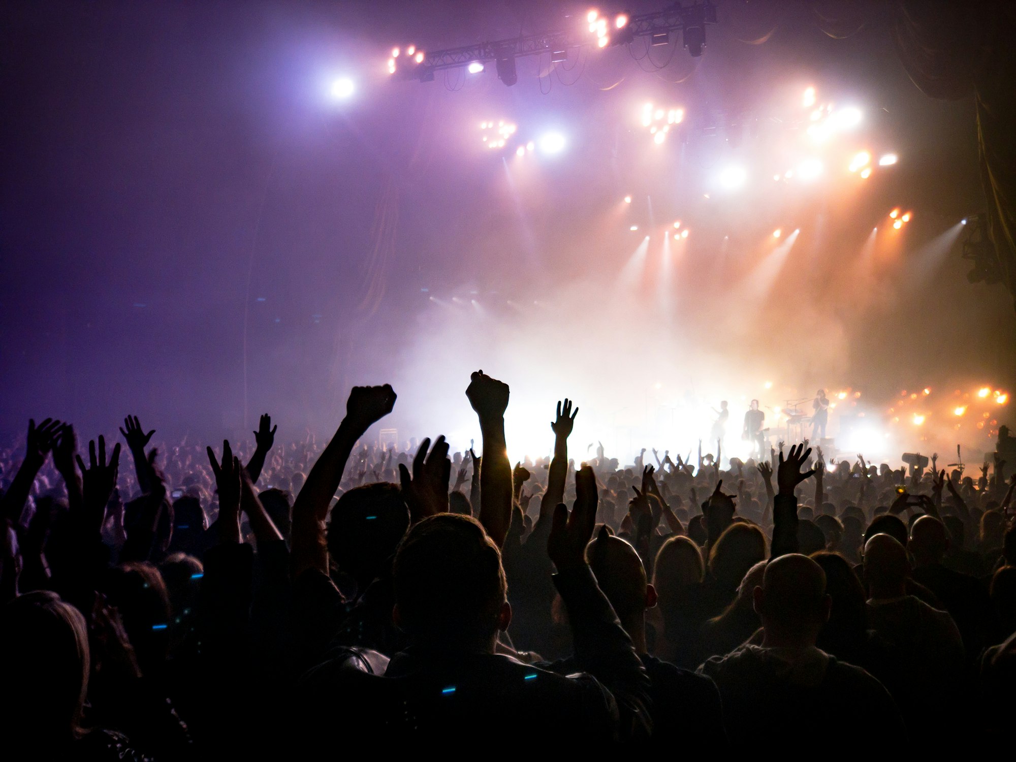 Hands raised in a crowd facing a lit stage
