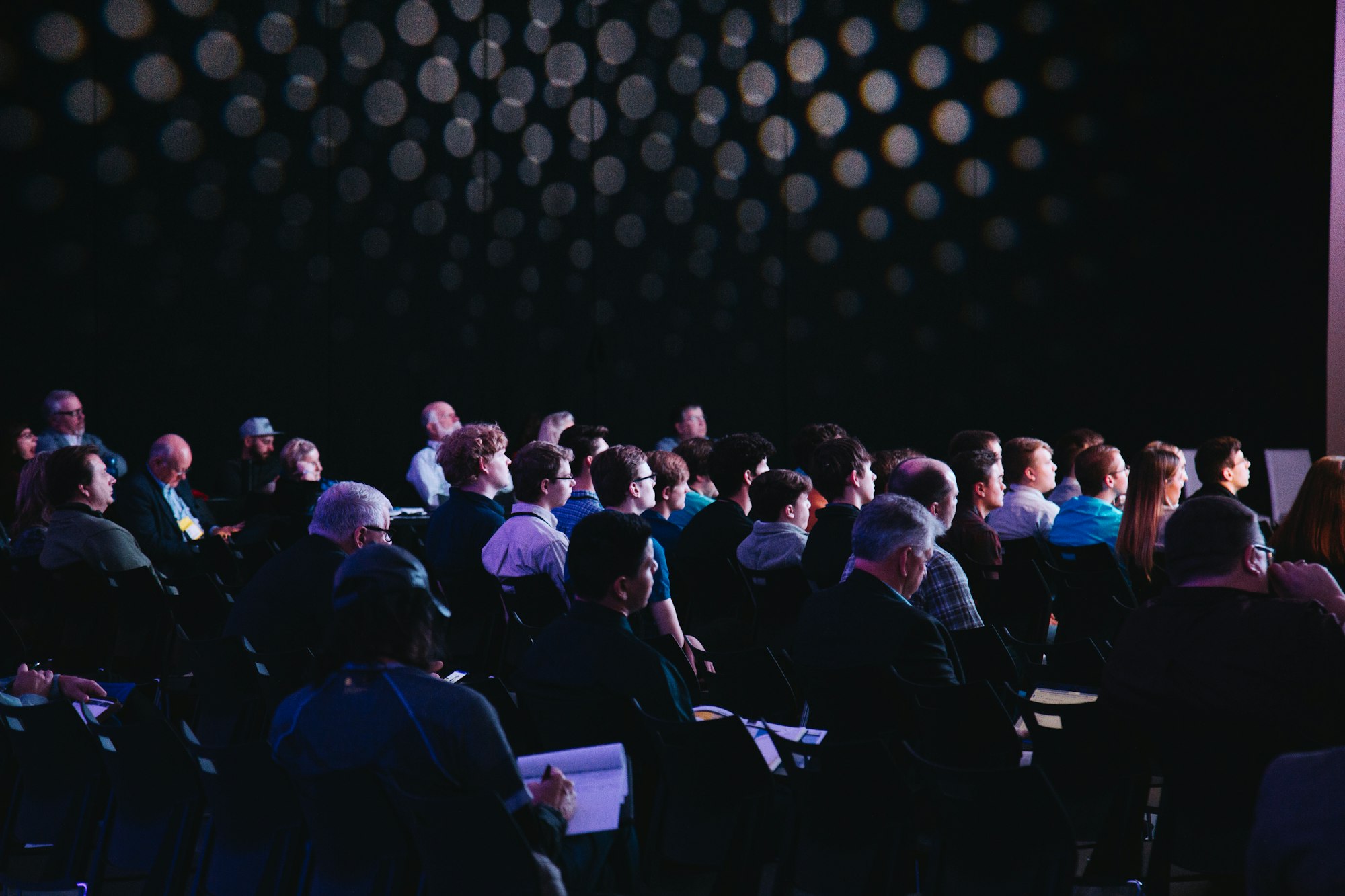 Corporate event: an attentive audience in a dark conference hall, seen from behind